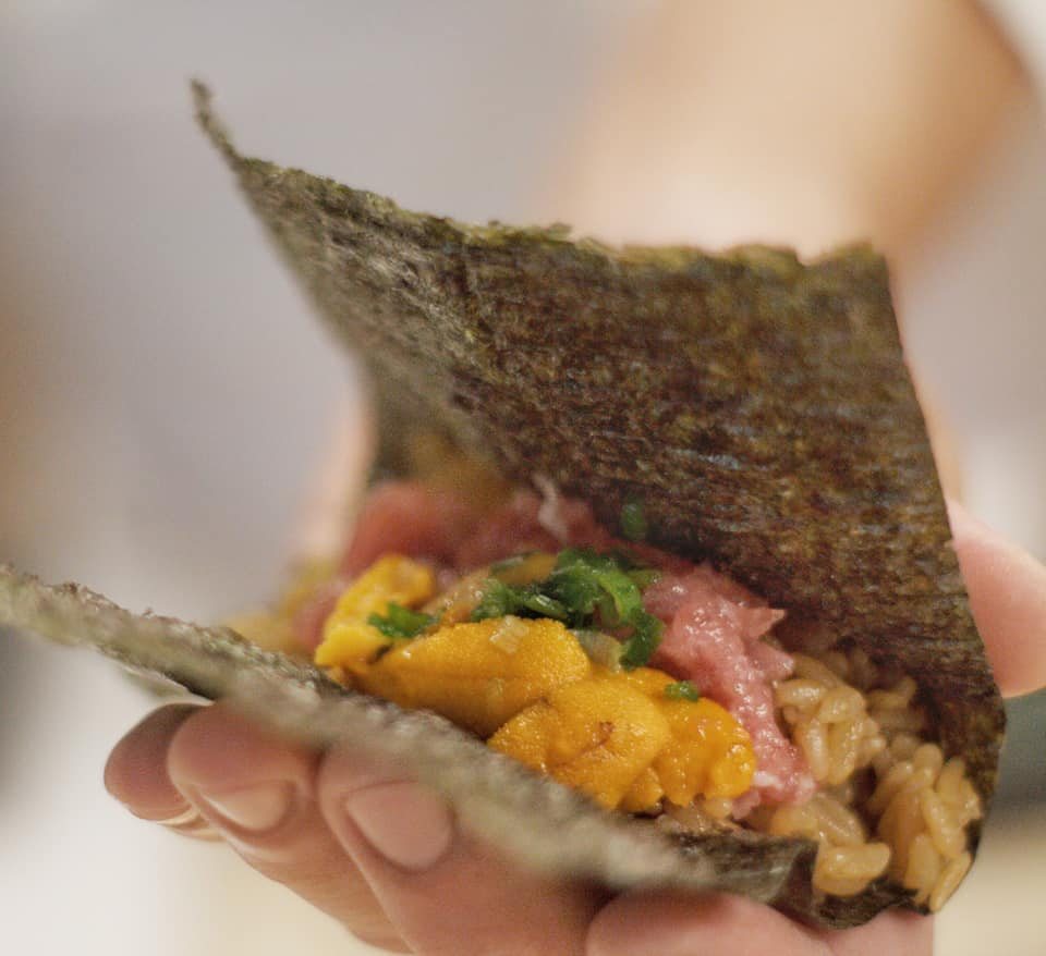 A hand-rolled temaki of sea urchin and wagyu being passed across the counter