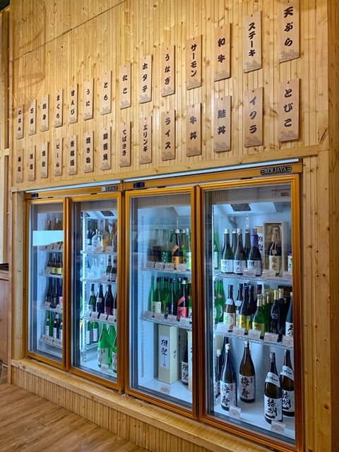 A wall of sake and shochu bottles in a glass-fronted fridge